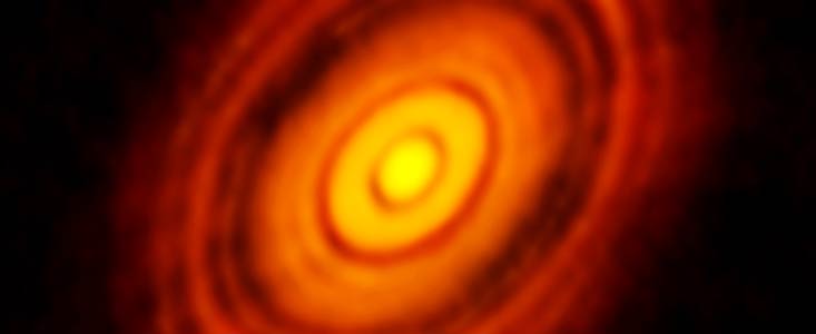 Hazy thick rings in a disc shape glow in contrast to a dark background. The rings are red near the edges and shift to shades of orange, then yellow, moving inwards.
