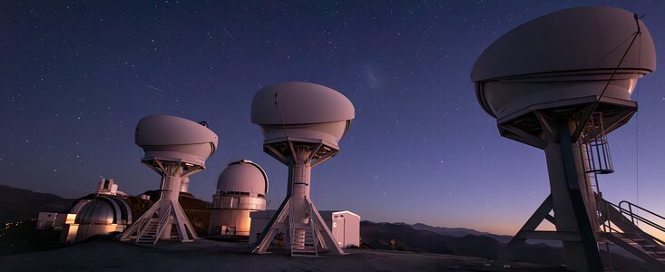This photograph shows, in the foreground, the three open domes of the telescopes of the BlackGEM array under a stunning night sky, while other telescopes at ESO's La Silla Observatory in Chile are visible in the background.