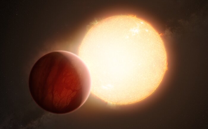 This image shows an artistic view of a bright yellow star and a large red planet, which partially obscures the star from the viewer. The side of the planet facing the star is brightly lit and the other side is in shadow. The gaseous atmosphere of the planet is visible and as a hazy glow around it.