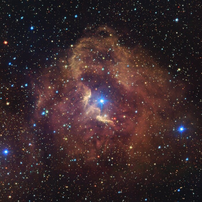 Dieses Bild zeigt den Nebel Gum 41, der den größten Teil des Bildes einnimmt. Es ist ein rötlich-brauner, kreisförmiger Nebel mit einem hellen Zentralstern. Ein zweiter heller Stern befindet sich außerhalb des Nebels unten rechts im Bild, umgeben von weiteren, schwächeren rötlich-braunen Wolken. Der Hintergrund des Bildes ist mit Sternen in vielen Farben und Größen übersät.